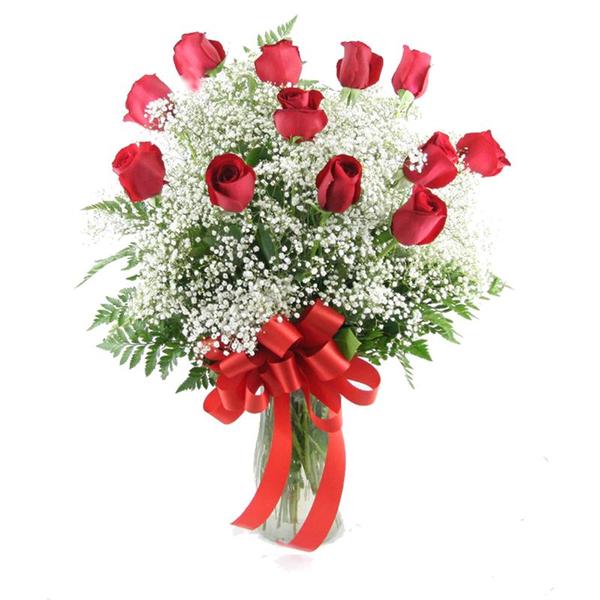 A dozen red roses, adorned with greenery and babies breath in a clear glass vase with a bow. 