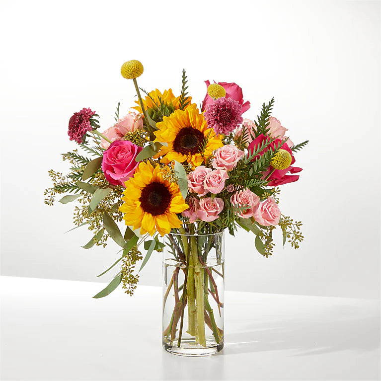 Bouquet of flowers with yellow sunflowers, light pink miniature roses and pink roses in a clear vase on a white background