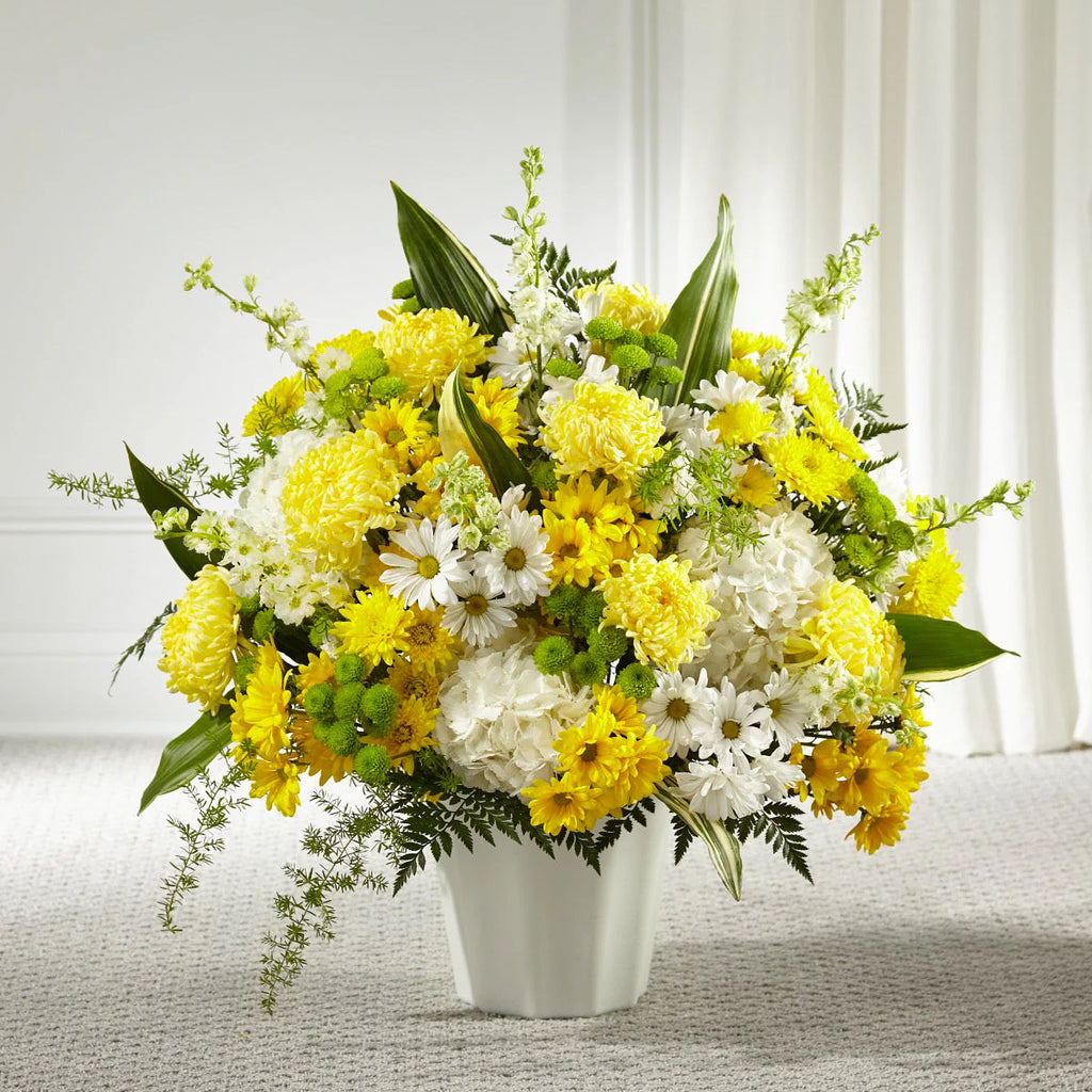 Sitting arrangement of yellow and white flowers with greenery in a white floor container. 