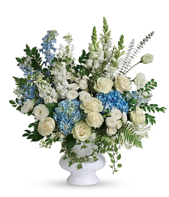 Floral arrangement with white and blue flowers in a white pastic urn on a white background