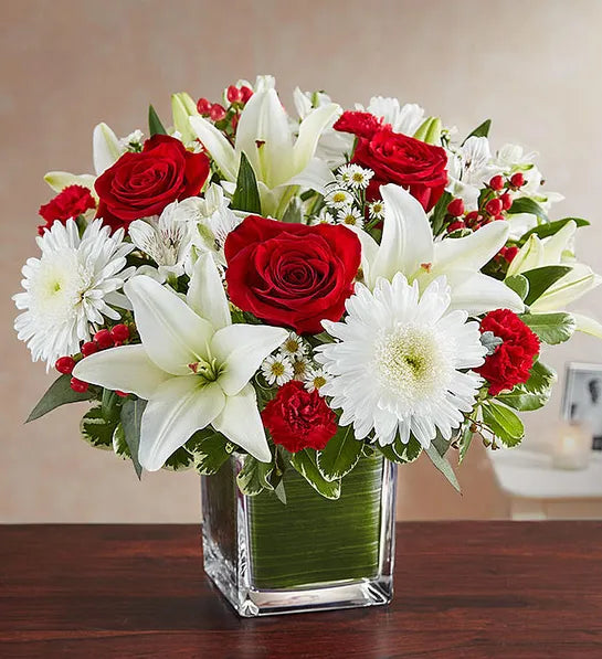 A square vase filled with a mix of red and white flowers, including roses and lilies, arranged to say 'I love you'.