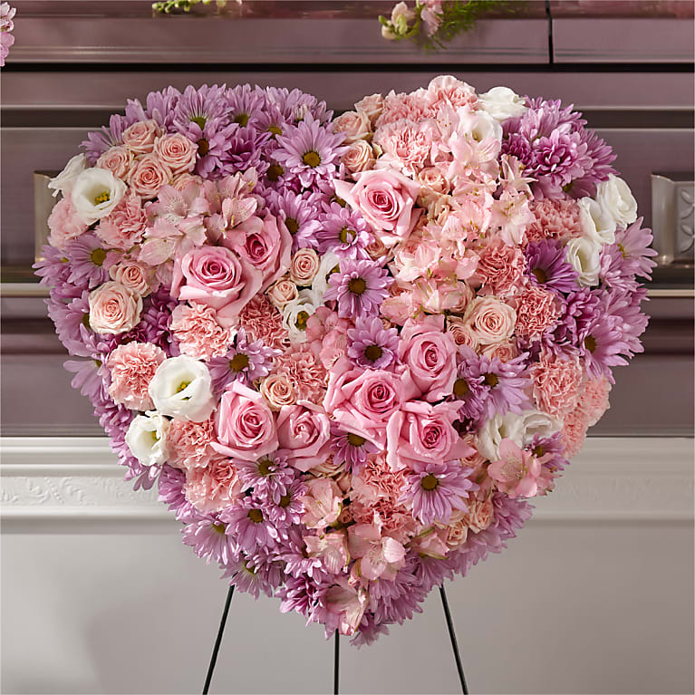 Solid heart-shaped arrangement with light pink, lavender and white flowers on a easel. 