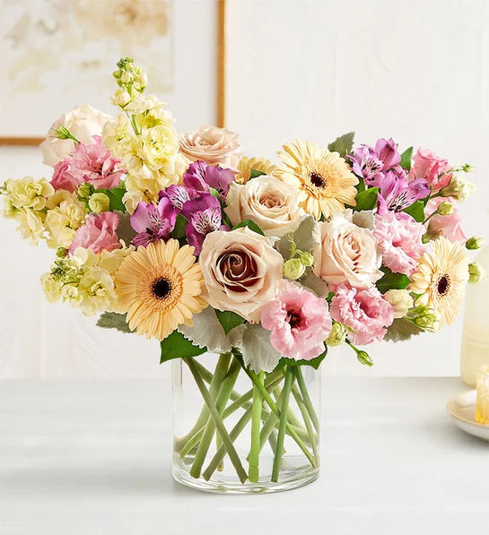 Bouquet of pastel flowers in a clear short cylinder vase on a light surface