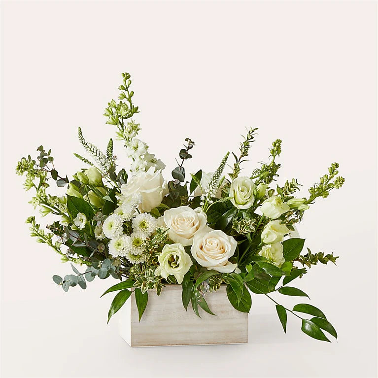 Floral arrangement with white flowers and greenry in a box on a light background