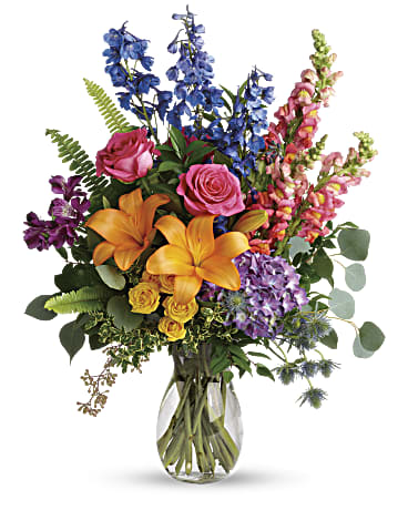 A clear vase filled with greenery and a variety of brightly colored flowers from hydrangeas to roses, everything under the rainbow.   Vase and/or flower variety will vary depending on availability. Arrangement will be as close as possible, but may not be exact.