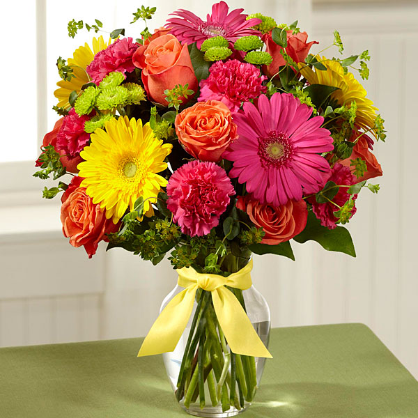 Hot pink, orange, lime green and yellow flowers such as roses, carnations, gerbera daisies and button mums are designed together in a clear glass vase.    Vase and/or flower variety will vary depending on availability. Arrangement will be as close as possible, but may not be exact.