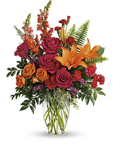 A clear vase filled with fuchsia and orange flowers. Orange snapdragons, orange lilies, orange miniature roses, hot pink roses and hot pink carnations.   Vase and/or flower variety will vary depending on availability. Arrangement will be as close as possible, but may not be exact.