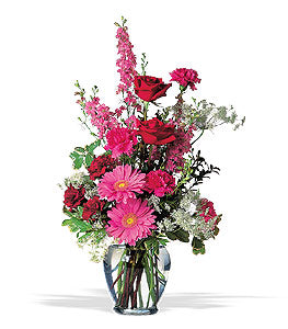 Clear vase filled with pink and red flowers such as roses, gerbera daisies, carnations, and larkspur.   Vase and/or flower variety will vary depending on availability. Arrangement will be as close as possible, but may not be exact. 