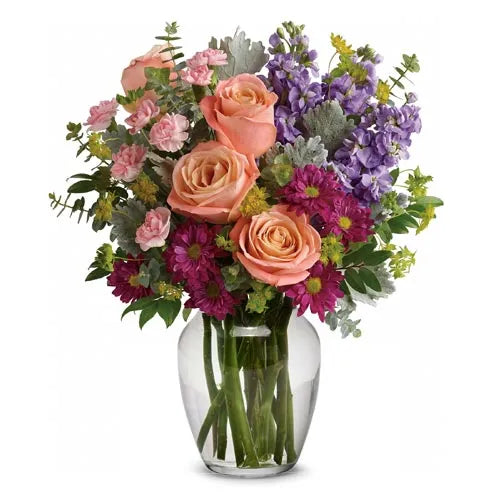 A clear vase filled with lavender, peach, and light pink assorted flowers.  Vase and/or flower variety will vary depending on seasonal availability. Arrangement will be as close as possible, but may not be exact. 